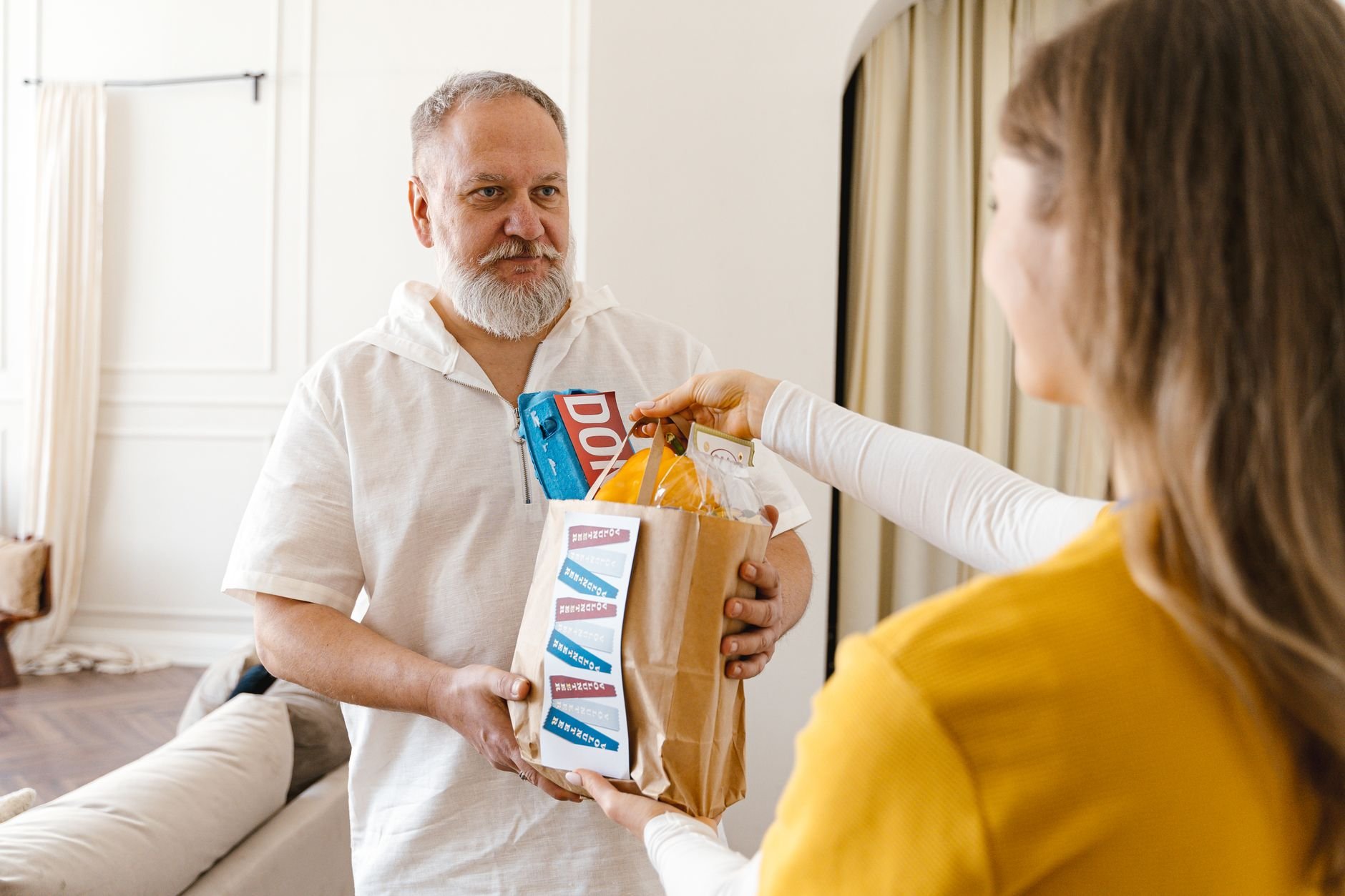An elderly man with a beard receiving a donation in a paper bag indoors, highlighting community support.